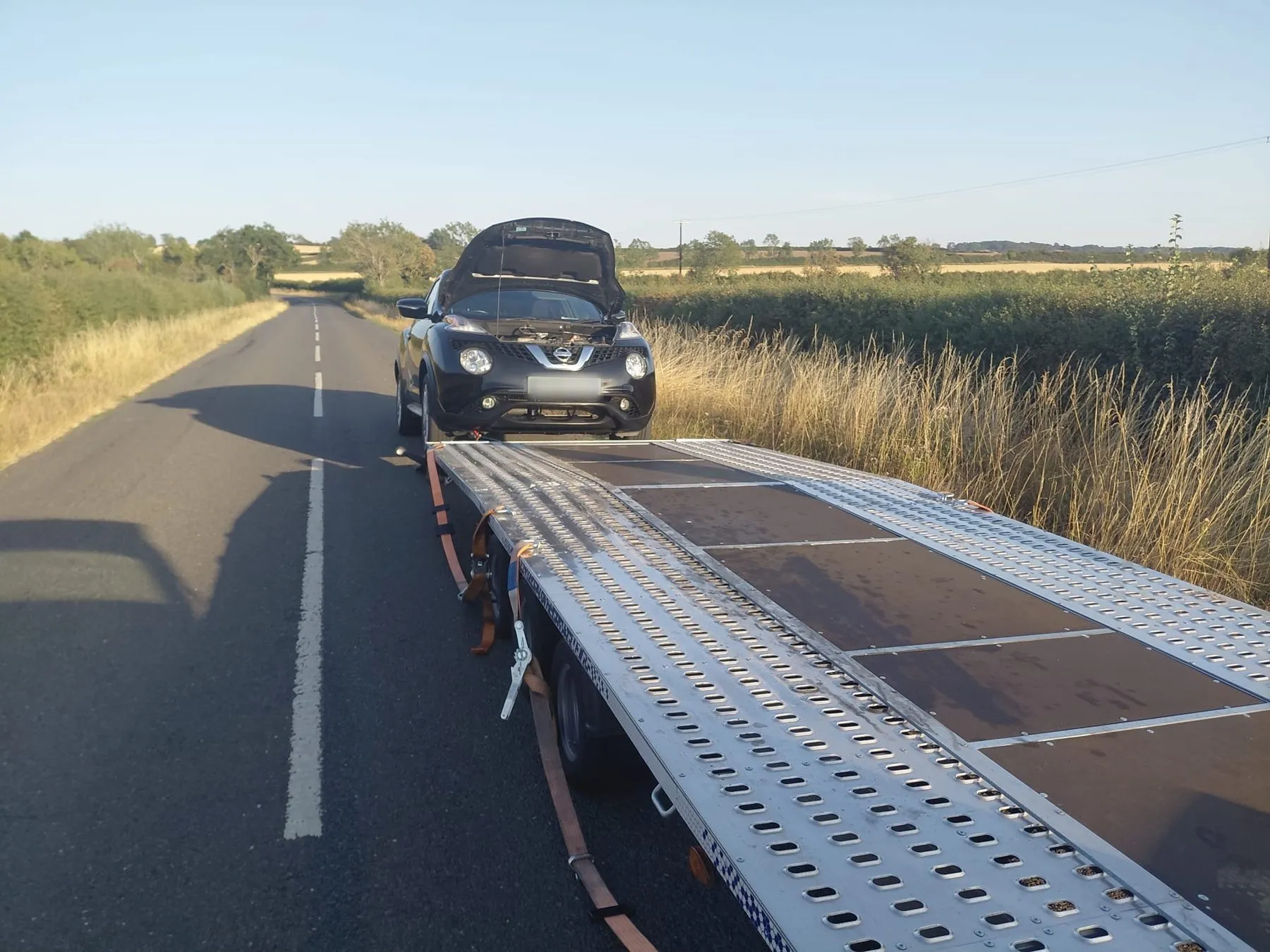 Broken-down Nissan with bonnet up being loaded onto the trailer on a country road
