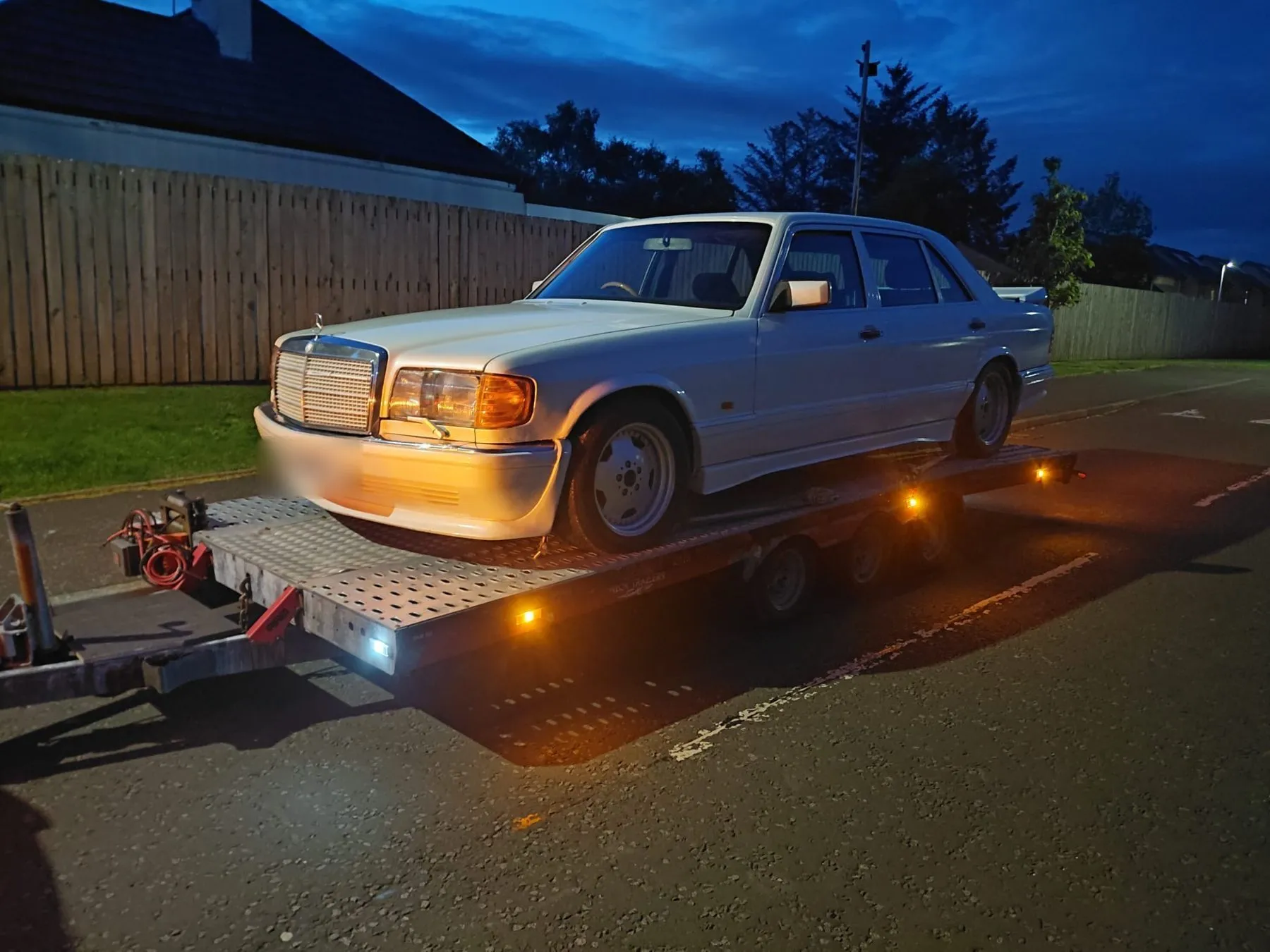 Car loaded on the VP Autos recovery trailer at dusk, amber beacons on